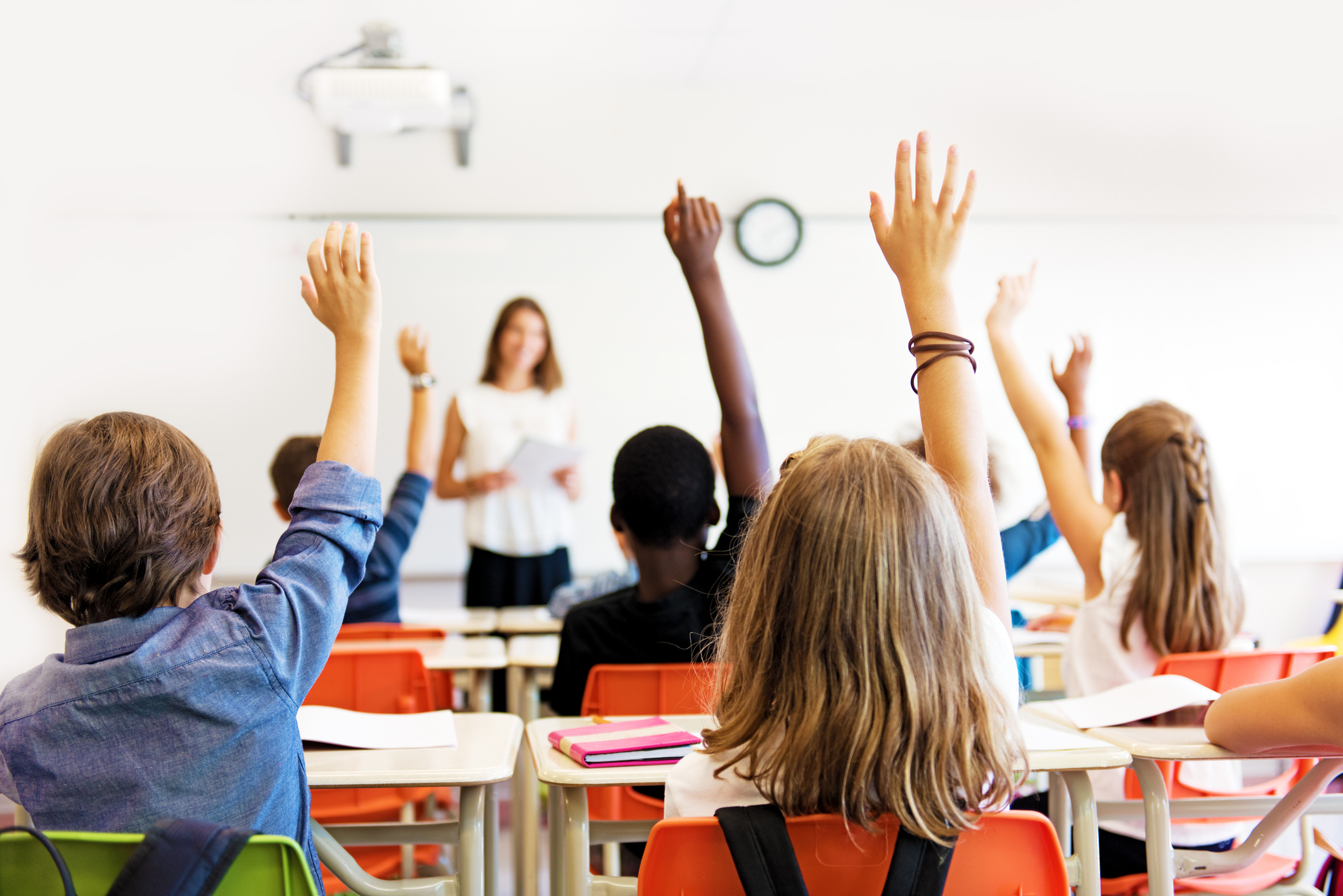School kids in classroom raising their hands